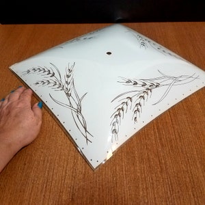May include: A square, white glass ceiling light shade featuring a black line-art pattern of wheat stalks in the corners and a small circular hole in the center. The edges of the glass shade are decorated with a series of small black dots.
