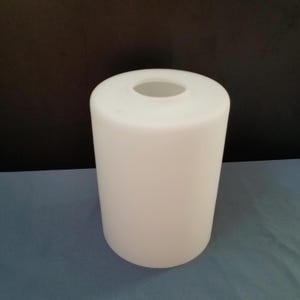 May include: A cylindrical, white lampshade with a rounded top and a circular opening. The lampshade is opaque and has a smooth surface. The background is a dark gray and blue.