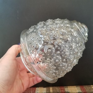 May include: Clear glass light fixture with a textured, bubble-like surface. The fixture has a rounded shape with a flared base and a decorative rim. The glass is transparent, allowing light to pass through.