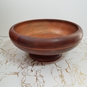 May include: A round, wooden bowl with a pedestal base. The bowl is a dark brown color with a lighter brown interior. A thin, lighter brown stripe encircles the bowl. The bowl is likely used for serving food or as a decorative item.