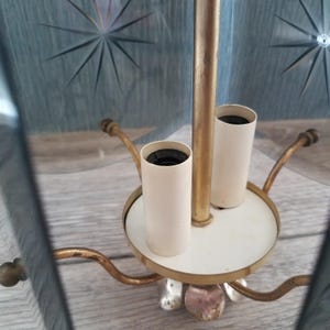 May include: Vintage brass and glass chandelier with starburst etched glass panels. The chandelier features a white base with two light sockets and decorative arms. The glass panels are a light blue color.
