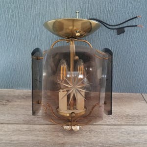 May include: Vintage brass and glass wall sconce with a starburst design. The sconce features a brass canopy, curved arms, and a clear glass shade with etched star details. The sconce has two light bulbs.