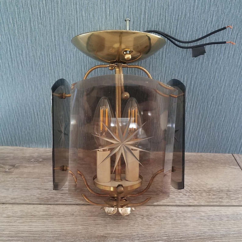 May include: Vintage brass and glass wall sconce with a starburst design. The sconce features a brass canopy, curved arms, and a clear glass shade with etched star details. The sconce has two light bulbs.