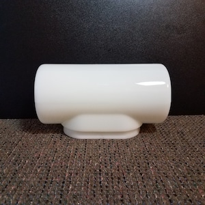 May include: A white, opaque glass light fixture with a cylindrical top and a rounded base. The fixture has a smooth, glossy finish and is designed to be mounted on a wall or ceiling. The fixture is likely for a bathroom or kitchen.