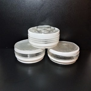 May include: Three vintage glass and white light fixtures. The fixtures have a round, tiered design with a textured glass bottom and a white band around the middle. The top fixture is clear glass. The fixtures are stacked on top of each other against a black background.