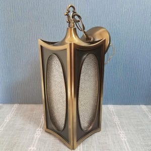 May include: Vintage brass and black hanging lantern with textured glass panels. The lantern has a decorative top and a chain for hanging. The frame is a dark color with brass trim. The glass panels are oval shaped.