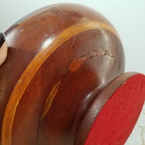 May include: A wooden decorative object with a dark brown finish and a lighter brown stripe. The base is red. The object has some imperfections in the wood.