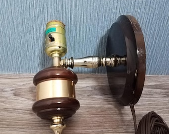 May include: A wall-mounted lamp fixture featuring a circular dark brown wooden base, a polished brass horizontal arm, and a central vertical component combining dark brown wood with brass accents. The light socket includes a small black toggle switch.