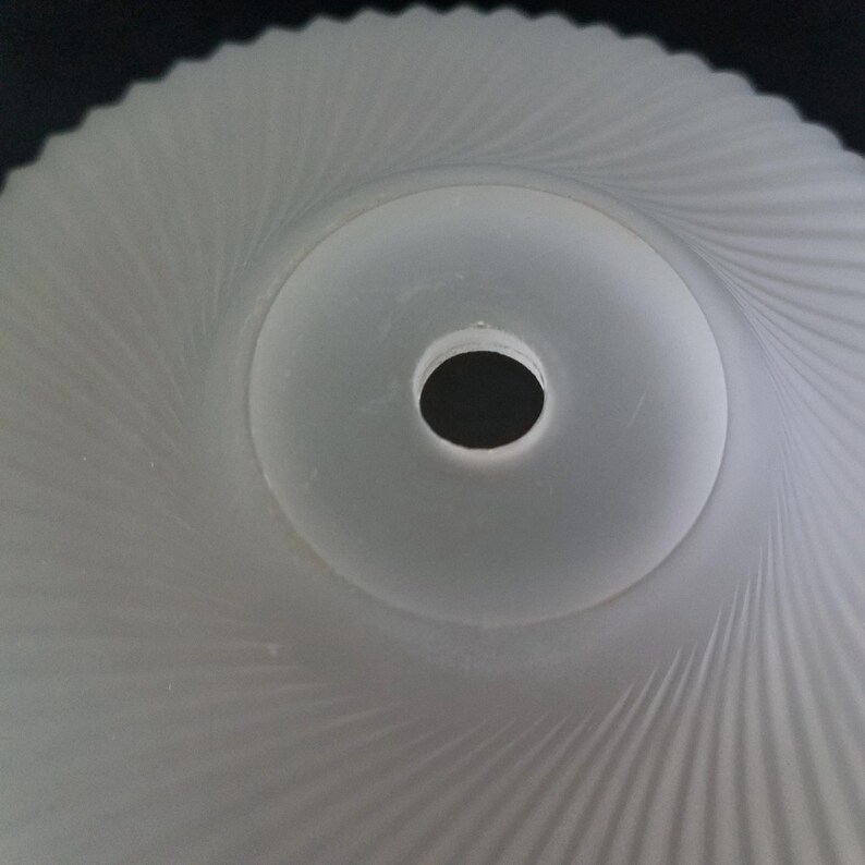 Może przedstawiać: Klosz lampy ze szkła matowego z spiralnym wzorem. Środek ma okrągły otw&oacute;r. Powierzchnia klosza ma teksturowany, żebrowany wz&oacute;r, kt&oacute;ry promieniuje na zewnątrz od środka. Og&oacute;lny kształt jest okrągły.