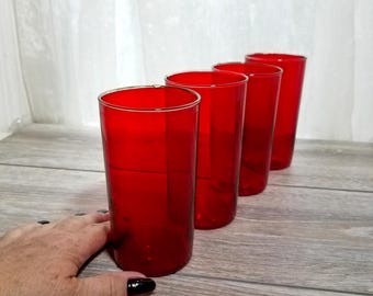 May include: Four tall, red drinking glasses arranged in a row. The glasses are made of a transparent material, allowing light to pass through. The glasses are on a wooden surface.
