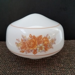 May include: A white glass light fixture globe with a rounded, dome-like shape. The surface features a printed floral design in shades of orange and yellow, depicting various flowers and leaves. A thin, horizontal orange line encircles the globe.
