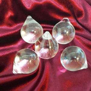 May include: Five clear glass decorative objects with a teardrop shape, arranged on a deep red velvet surface. The glass reflects light, creating highlights and shadows. The objects are likely for home decor or artistic display.