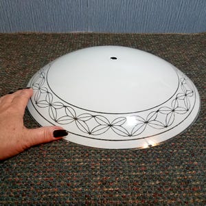 May include: White glass lampshade with a black floral pattern around the edge. The lampshade is dome-shaped and has a single hole at the top. The design is a simple, elegant style.