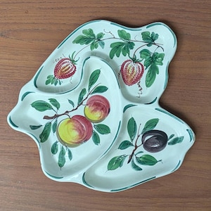 May include: A white ceramic serving platter with three sections, featuring hand-painted fruit illustrations. The design includes red strawberries, yellow and red peaches, and a dark plum, all with green leaves and vines. The platter has a green border.