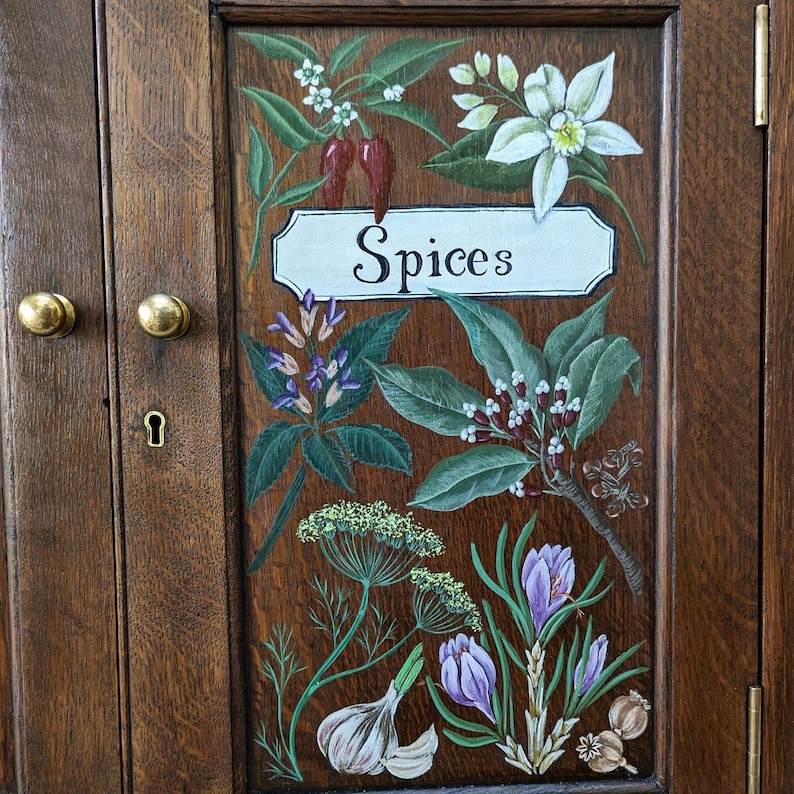 May include: A wooden cabinet door with a painted design of various spices and herbs. The door is painted in a dark brown wood grain pattern. The words "Spices" are painted in white on a white rectangular sign.