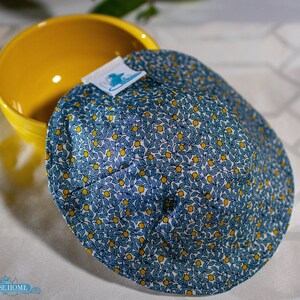 May include: A blue and yellow fabric bowl cozy with a lemon print. The cozy is sitting on top of a yellow bowl.