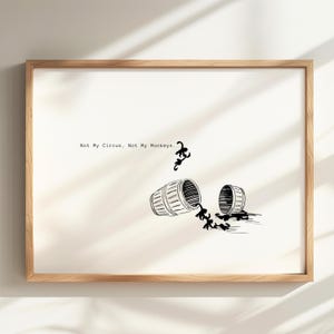 May include: A framed wall art print featuring a white background with black line art of a barrel split into two pieces. Small black monkey silhouettes are depicted emerging from the barrel. The text reads, Not My Circus, Not My Monkeys.
