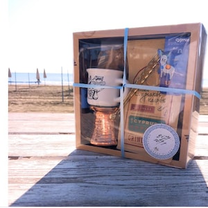 May include: A gift box set containing a white ceramic coffee cup with a Greek design, a copper coffee pot, and a bag of Greek coffee. The box is decorated with a blue and white Greek key design and the text "Cyprian Coffee".