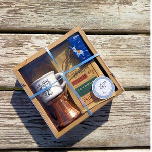 May include: A gift box set for making Greek coffee. The set includes a small white ceramic mug with a donkey design, a copper cezve, and a bag of Cyprus coffee.
