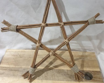 Puede incluir: Una estrella de cinco puntas hecha de ramitas trenzadas, atadas con cuerda. La estrella está apoyada sobre una superficie de madera.