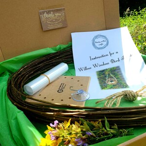 Peut inclure: Un kit pour fabriquer un nichoir &agrave; oiseaux en saule &agrave; poser sur une fen&ecirc;tre. Le kit comprend un fagot de branches de saule, une ventouse, un morceau de ficelle, une base en bois avec des trous, un tube en plastique transparent et des instructions. Le kit est pos&eacute; sur une surface verte avec quelques fleurs.