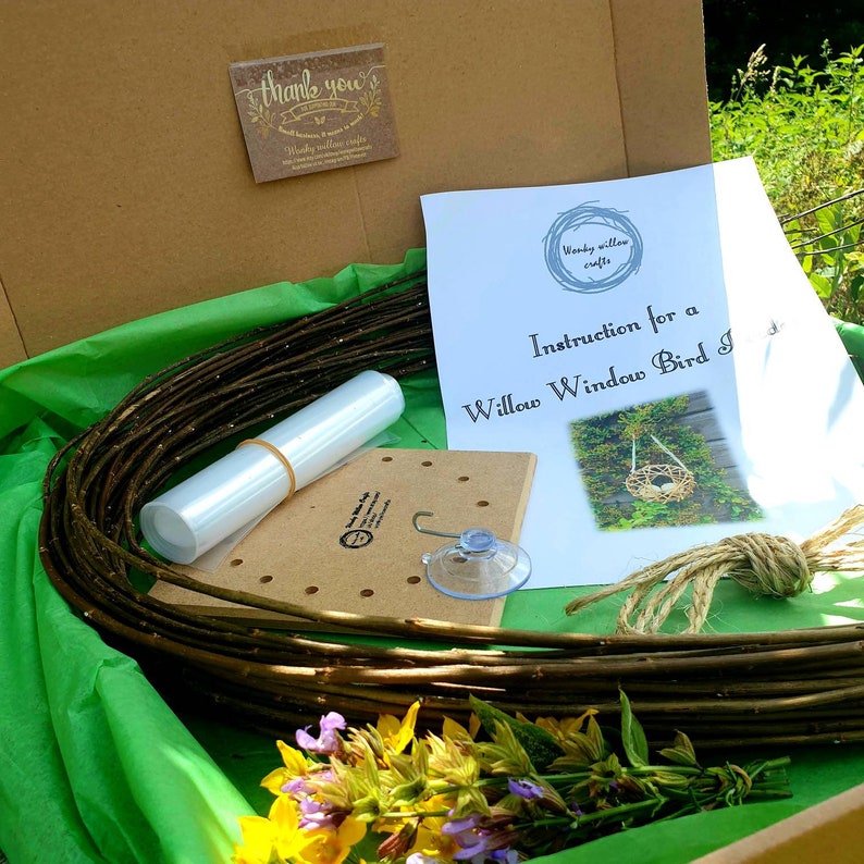 Peut inclure: Un kit pour fabriquer un nichoir &agrave; oiseaux en saule &agrave; poser sur une fen&ecirc;tre. Le kit comprend un fagot de branches de saule, une ventouse, un morceau de ficelle, une base en bois avec des trous, un tube en plastique transparent et des instructions. Le kit est pos&eacute; sur une surface verte avec quelques fleurs.