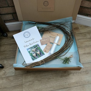 K&ouml;nnte beinhalten: Ein Bastelset zum Herstellen von Weidenvogelh&auml;uschen. Das Set enth&auml;lt Weidenzweige, Anleitungen und eine Plastikt&uuml;te. Das Set ist in einer braunen Pappebox mit blauem Seidenpapier verpackt.