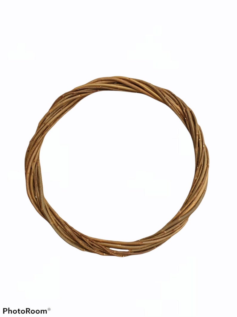 Puede incluir: Una corona de ramas marrones con un acabado de purpurina dorada. La corona es circular y tiene un di&aacute;metro de aproximadamente 30 cm.