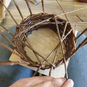 Peut inclure: Un panier en osier en cours de fabrication, fait de brindilles brunes. Le panier est rond et a une base plate. Le panier est tiss&eacute; &agrave; la main.