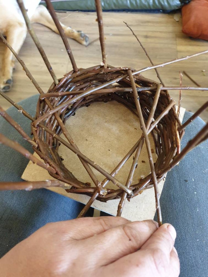 Peut inclure: Un panier en osier en cours de fabrication, fait de brindilles brunes. Le panier est rond et a une base plate. Le panier est tiss&eacute; &agrave; la main.