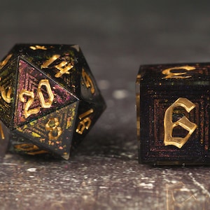 Könnte beinhalten: Zwei polyedrische Würfel für Tischspiele. Einer ist ein 20-seitiger Würfel, der andere ein 6-seitiger Würfel. Beide sind schwarz mit goldenen Zahlen. Der 20-seitige Würfel hat ein schimmerndes, irisierendes Inneres mit lila und grünen Farbtönen. Der 6-seitige Würfel hat eine goldene Zahl 6.