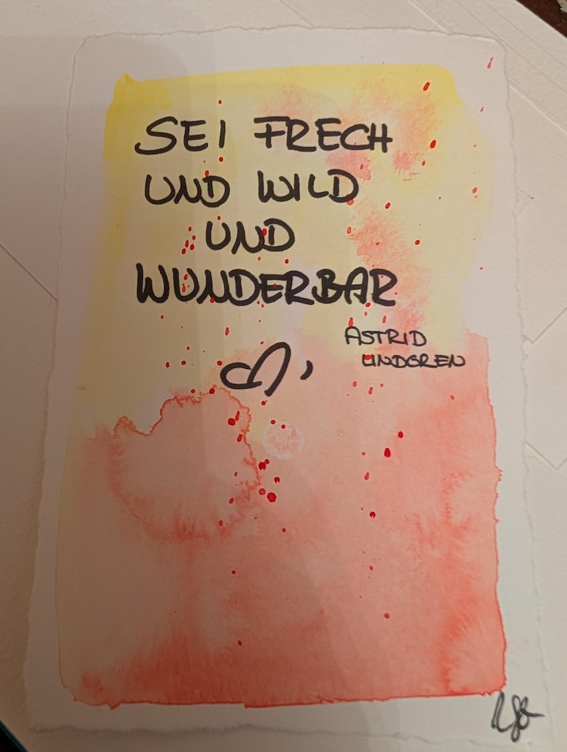 Puede incluir: Obra de arte en acuarela con el texto alem&aacute;n "SEI FRECH UND WILD UND WUNDERBAR" en negro, con un s&iacute;mbolo de coraz&oacute;n y el nombre "ASTRID LINDGREN". El fondo presenta un degradado de amarillo y naranja con salpicaduras de pintura roja.