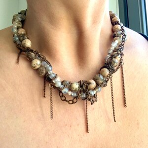 May include: A layered necklace with brown and white beads, metal chains, and dangling metal strands.