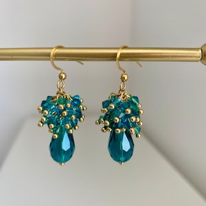 Può includere: Un paio di orecchini pendenti dorati con perline di cristallo blu turchese e un cristallo a forma di lacrima nella parte inferiore.