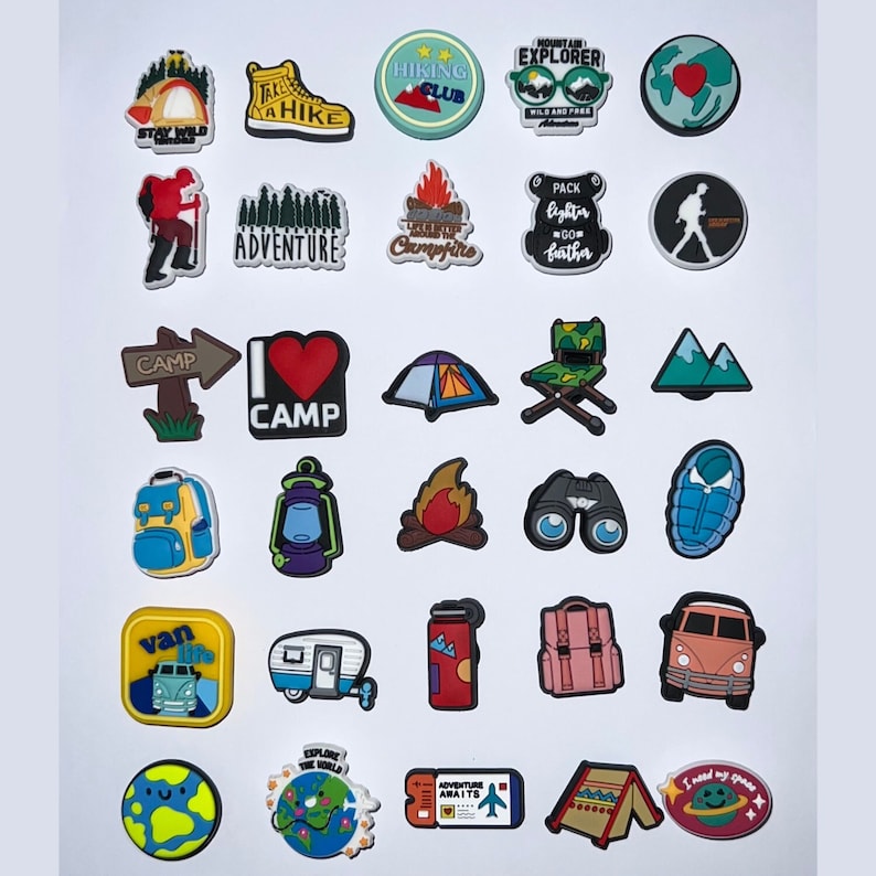 May include: A collection of camping-themed charms in various shapes and colors. Designs include a tent, campfire, hiking boot, backpack, and phrases like "Adventure Awaits" and "Stay Wild." These charms are ideal for personalizing shoes or accessories.