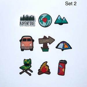 May include: Set of nine camping-themed charms. Includes a forest with the word "Adventure", a globe with a heart, mountains, a camper van, a "Camp" sign, a tent, a folding chair, a campfire, and a red thermos.