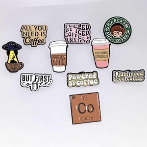 May include: A selection of coffee-themed enamel pins with diverse designs and text. Pins feature phrases such as "All You Need Is Coffee," "Fueled by Coffee & Anxiety," and "But First, Coffee." Other pins depict coffee cups and a periodic table element.