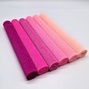 May include: Seven rolls of crepe paper in shades of pink and purple. The colors range from deep magenta to light peach. The paper has a textured, crinkled surface and is rolled up tightly. Ideal for crafting and decorative projects.