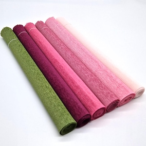 Könnte beinhalten: Eine Auswahl an gerolltem Krepppapier in Grün-, Burgunder- und Rosatönen. Die Rollen sind diagonal angeordnet und zeigen die verschiedenen Farben und Texturen. Das Papier ist eng gerollt und eignet sich für Bastelprojekte.