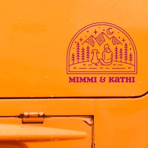 May include: A pink and white sticker with a line drawing of a person and a dog sitting in front of a mountain range with trees and stars. The text "MIMMI & KATHI" is below the drawing.