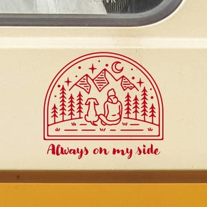 May include: Red line art sticker of a person and a dog sitting in front of a mountain range with stars and a crescent moon. The text "Always on my side" is below the image.