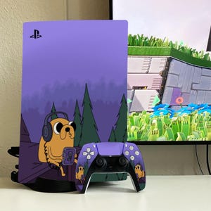 May include: A purple PlayStation 5 console and controller set. The console and controller are decorated with a cartoon image of a yellow dog wearing headphones. The console has a purple forest scene background.