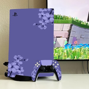 May include: A purple PlayStation 5 console with a floral design and a matching purple controller. The console has a PlayStation logo on the front.