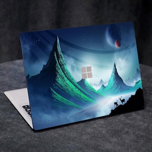 May include: A laptop computer with a blue and green mountain landscape design on the lid. The design features a ring of stars and a red planet in the sky. Two deer are standing in the foreground.