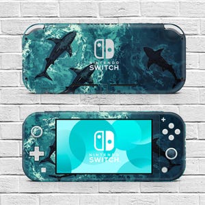 May include: A Nintendo Switch Lite console featuring a custom skin with a dark teal ocean water pattern and multiple shark silhouettes. The device displays the Nintendo Switch logo on the screen and the back casing, with standard buttons and joysticks.