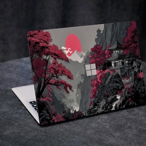 Può includere: Laptop con una skin personalizzata raffigurante un paesaggio di ispirazione giapponese. Il design include un sole rosso, montagne, una pagoda e alberi con foglie rosse su sfondo grigio. Il laptop è aperto, mostrando la tastiera.
