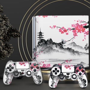 May include: Two black and white PlayStation 4 controllers with a Japanese cherry blossom design. The controllers are on a white background with a black and white image of a Japanese pagoda and cherry blossoms.