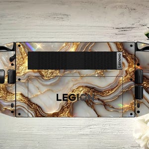 Può includere: Una skin per dispositivo di gioco Lenovo Legion con un design a marmo bianco e oro. La skin ha una presa d'aria nera e il logo Lenovo. La parola "LEGION" è stampata sul dispositivo.