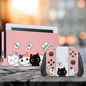 May include: Pink Nintendo Switch console and controller with a cute cat design. The console has a pink and white design with four cats on it. The controller has a white and pink design with three cats on it. The cats are all wearing different expressions and have different colored fur. The text "Hi", "Hello!" and a heart are on the console. The text "Hello!" and "Hi" are on the controller.