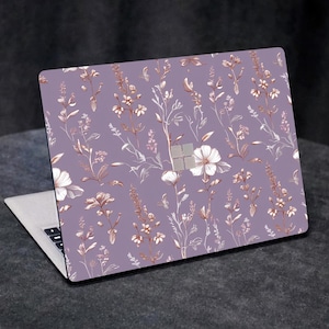 May include: A laptop computer with a floral design on the lid. The design features white flowers and gold-colored stems on a purple background.